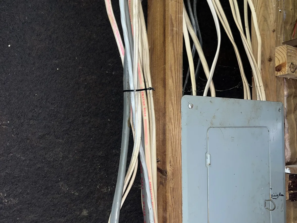 Bundles of cable run down the wall framing beside a breaker panel