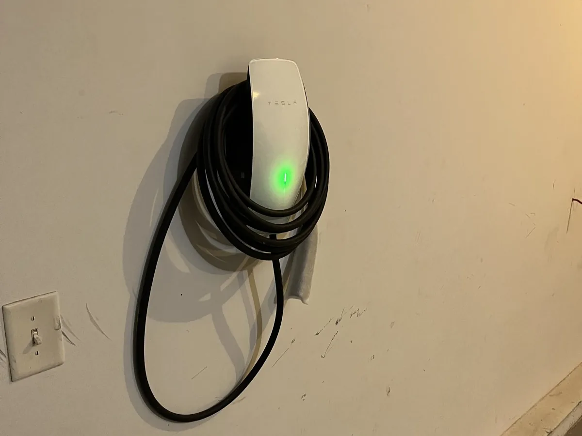 Tesla Wall Connector EV charger mounted on a wall, its cable coiled