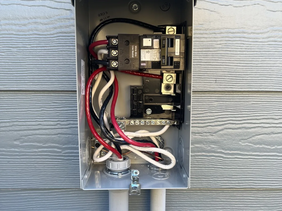 Open hot tub disconnect box with its GFCI breaker, wired on the side of a house