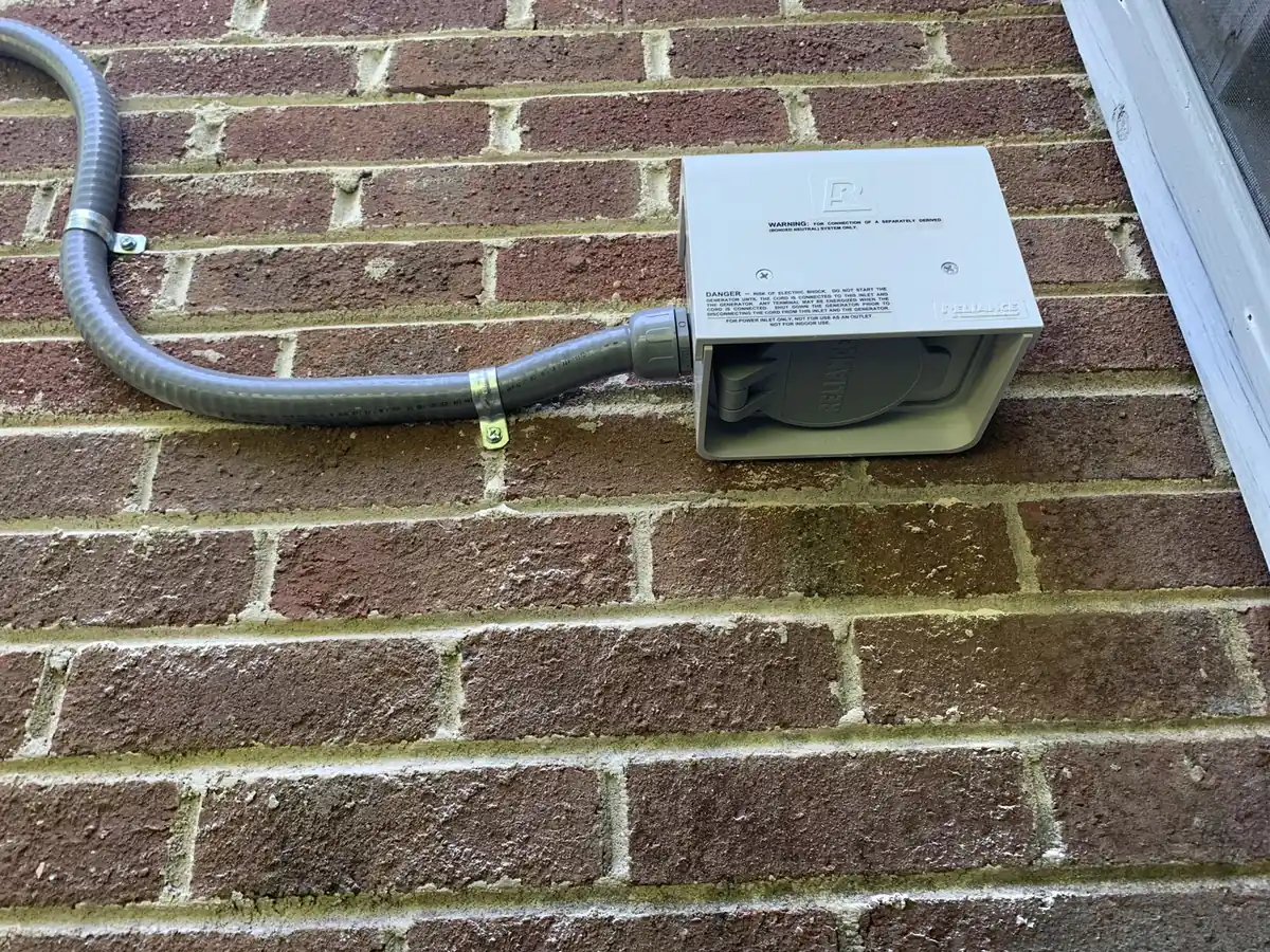 A generator power inlet box on a brick wall, wired to the panel through flexible conduit