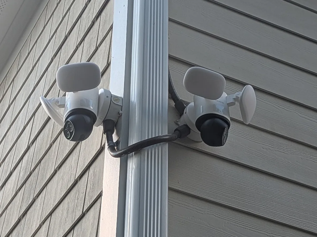 Two floodlight security cameras mounted on a downspout at the corner of a house