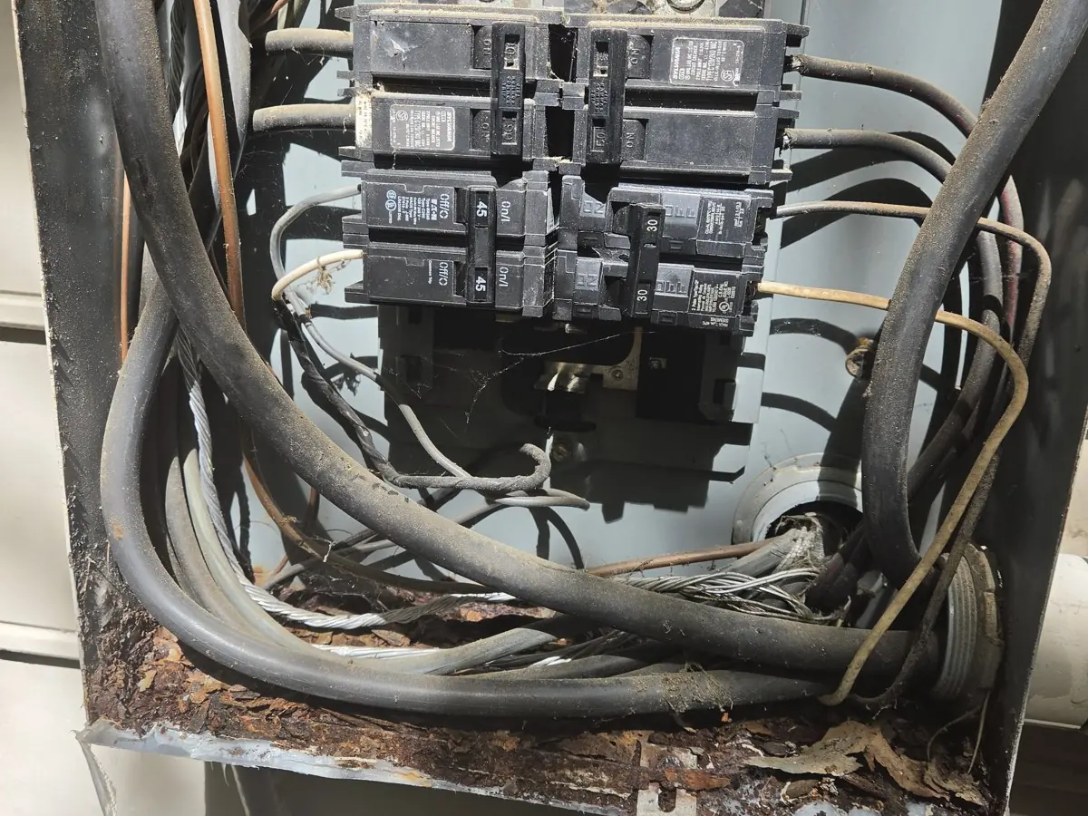 A dirty, cluttered electrical panel with exposed wires and rusted metal, in Oakwood, Raleigh