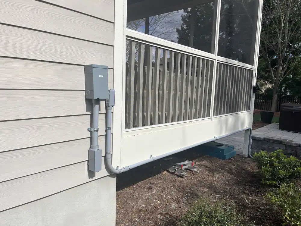Gray electrical disconnect mounted on light-colored house siding beside a screened porch in Oakwood, Raleigh