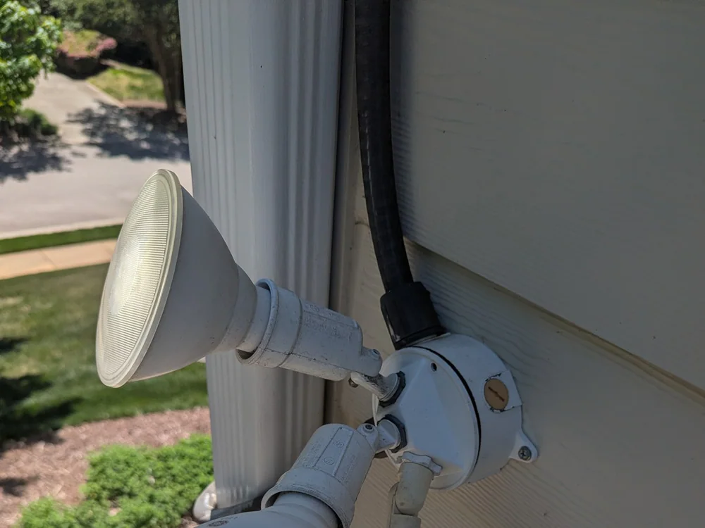 Two outdoor security floodlights mounted on a house wall, one lit and one off, in Budleigh, Raleigh