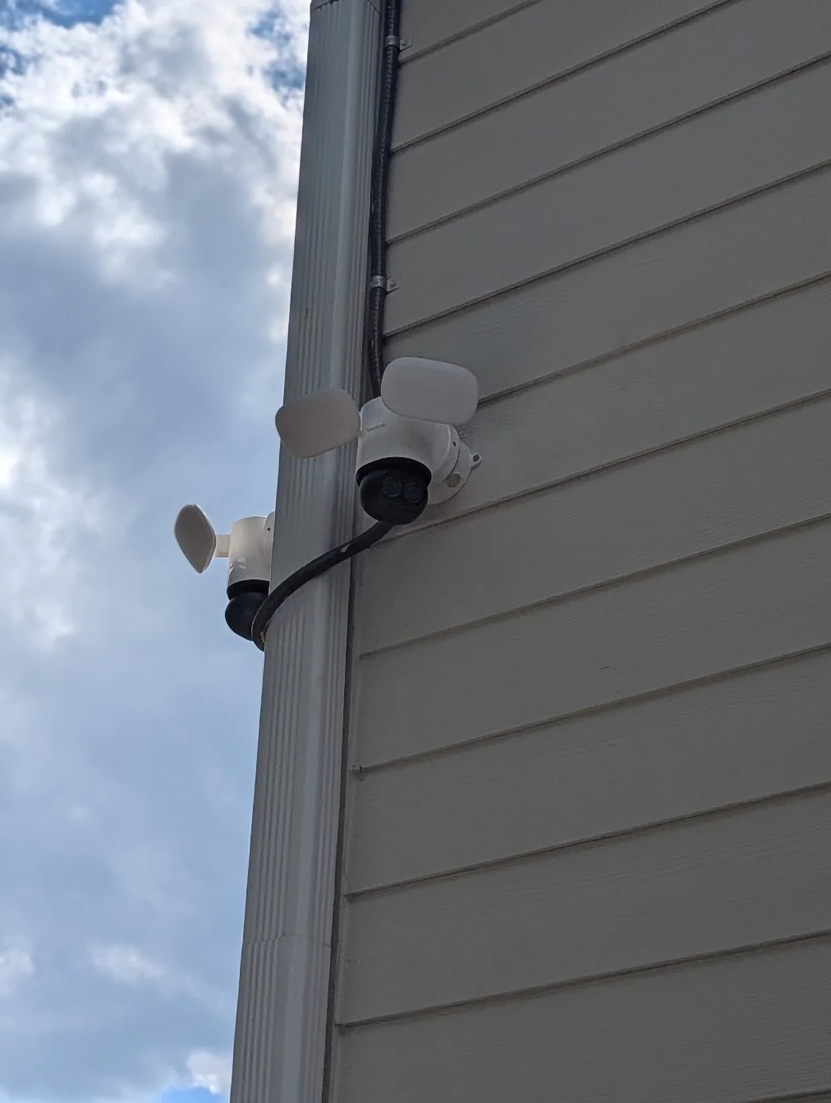 Two white outdoor security cameras mounted on house siding with cables running up the wall, in Budleigh, Raleigh