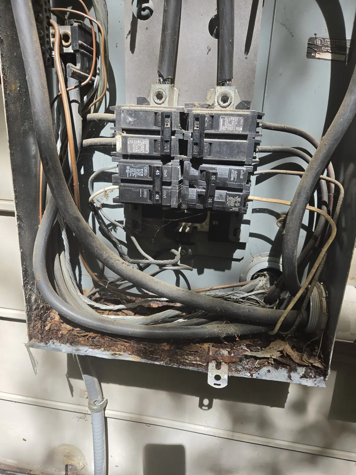 A dirty, cluttered electrical panel with exposed wires and rusted metal, in Oakwood, Raleigh