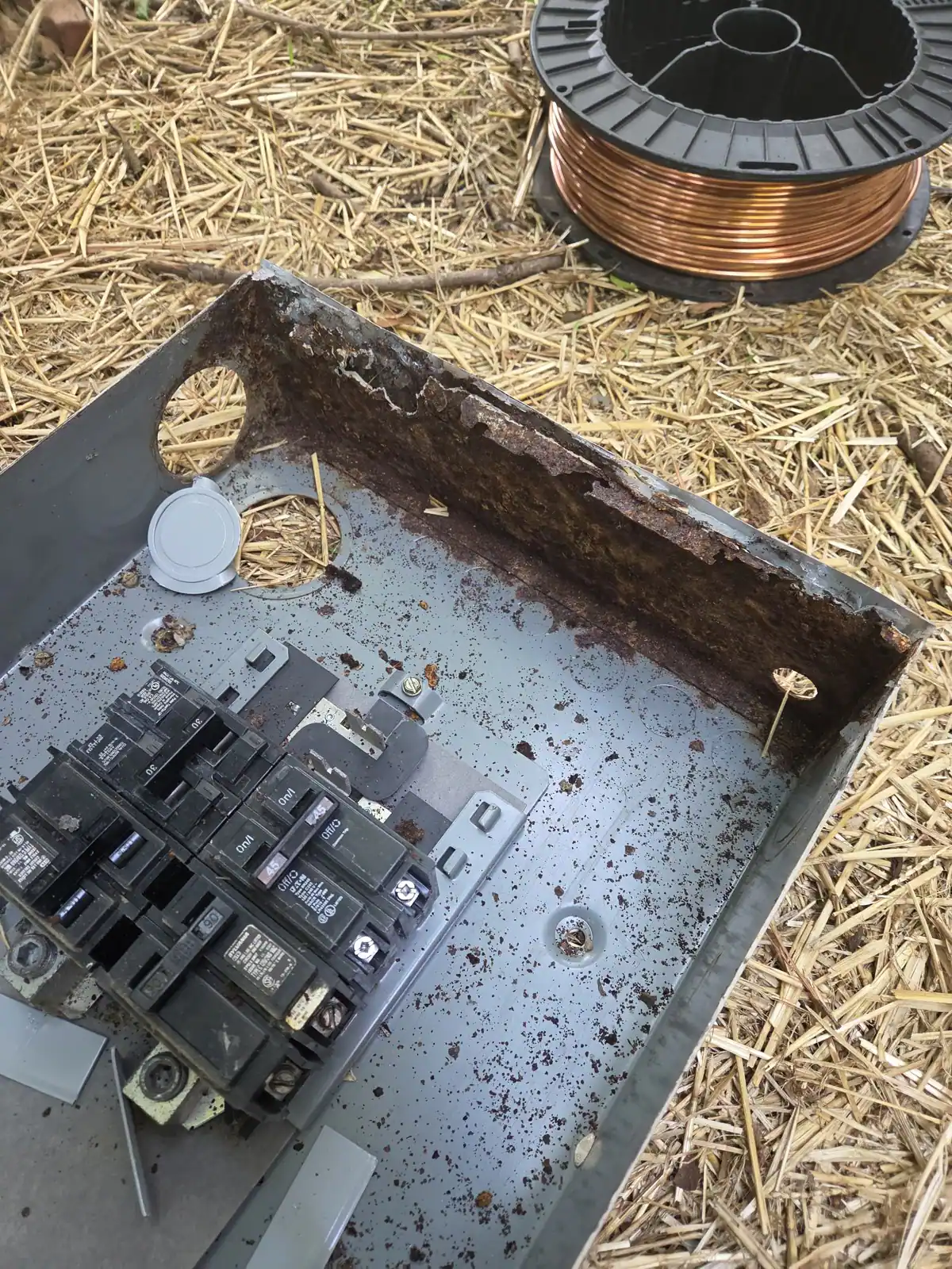 A rusted electrical panel with a broken cover and exposed breakers lying on the ground, in Oakwood, Raleigh