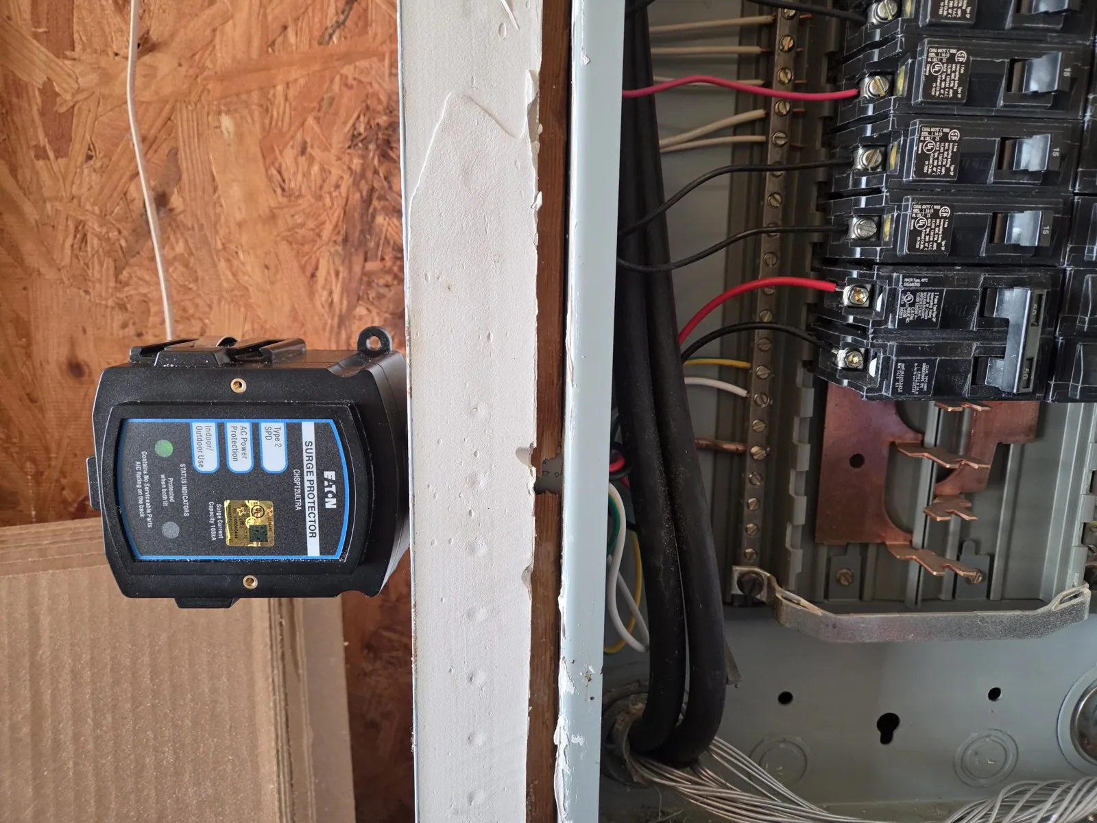 Surge protector installed next to an electrical panel, with wires and breakers visible, in Wakefield, Raleigh