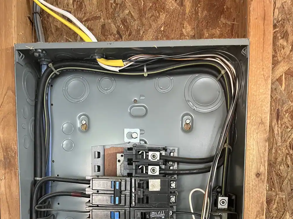 An open electrical panel set in a wooden enclosure, with wires and breakers exposed, in Oakwood, Raleigh
