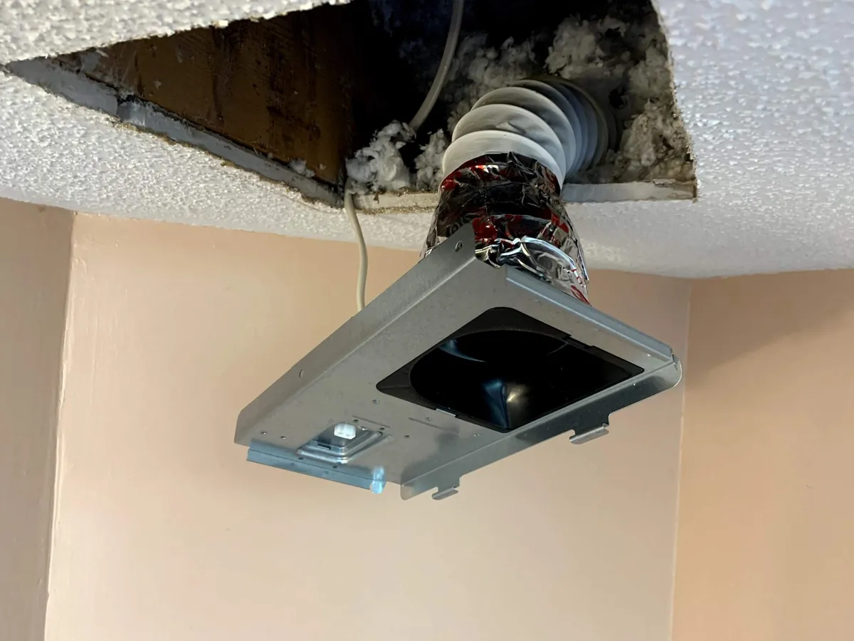 New bathroom exhaust fan housing being installed in the ceiling with its duct connected, by Electric All Pro in Raleigh, NC
