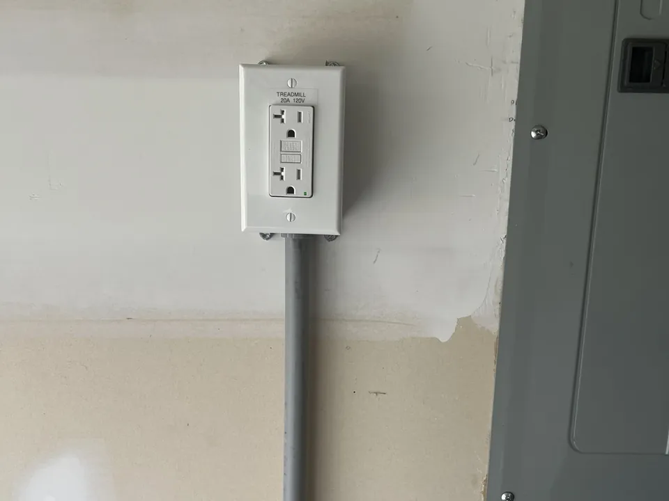 Dedicated 20-amp outlet installed on conduit beside an electrical panel