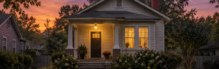 Small early-1900s mill house, porch light on at dusk